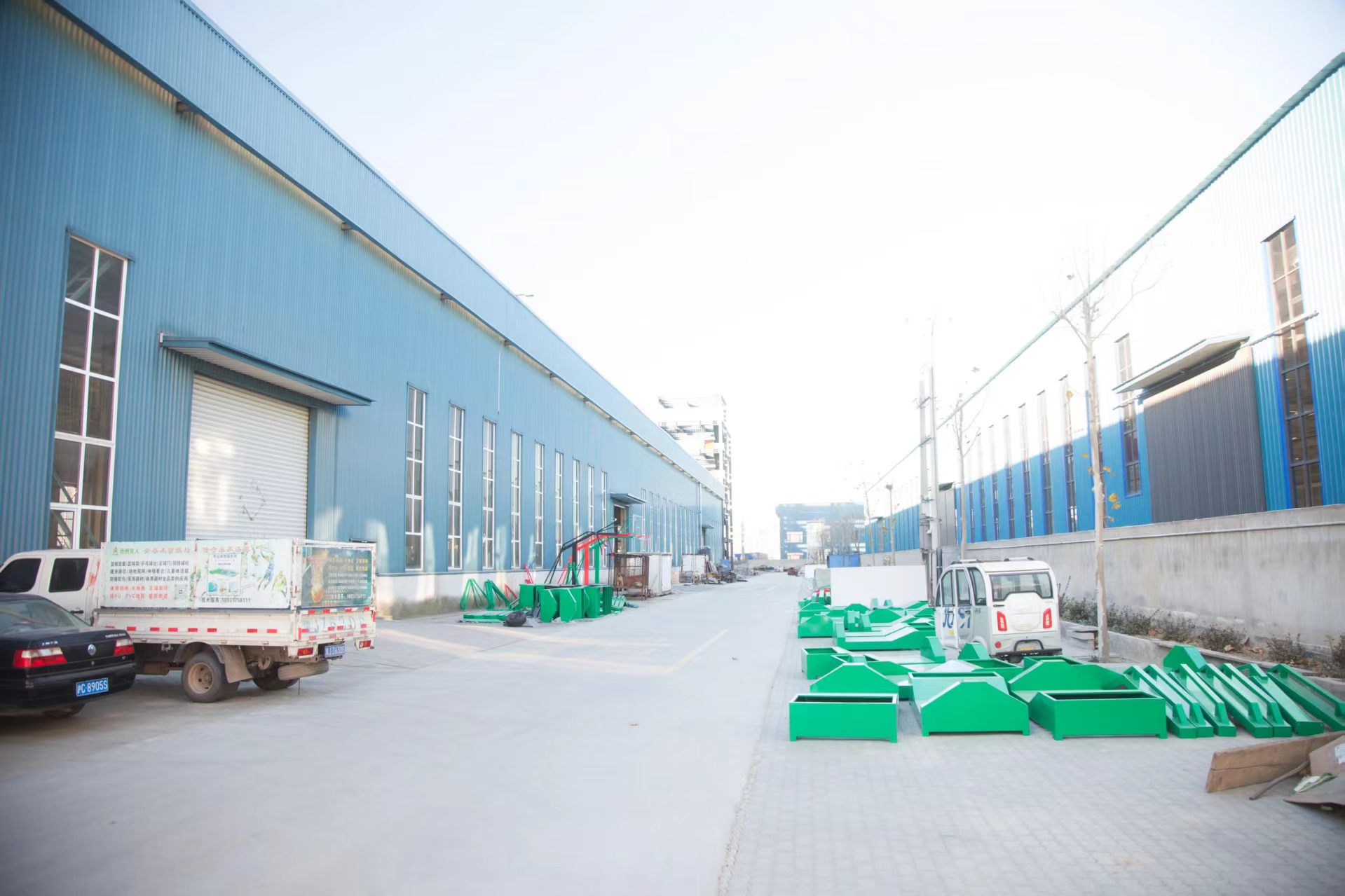 Blue factory buildings with a central driveway and green equipment components outside.