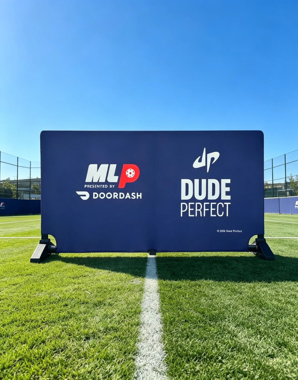 Blue printed court barrier on an outdoor turf court.